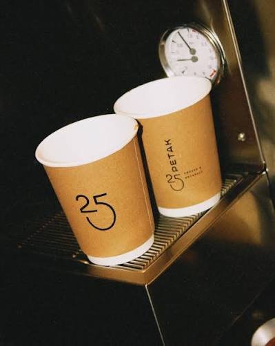 Dua gelas kertas kraft untuk dibawa pulang di atas mesin espresso, dengan jam dinding di belakangnya